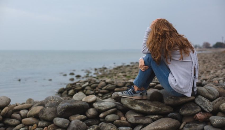 A girl sitting on rocks near the ocean.