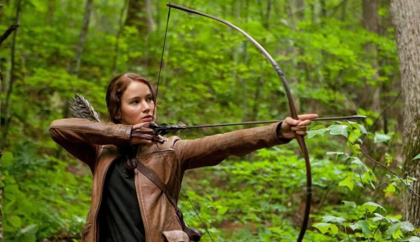 A woman is aiming a bow in the woods.