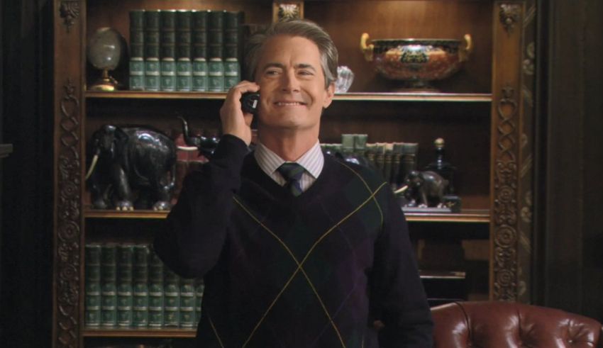 A man in a sweater and tie talking on the phone.