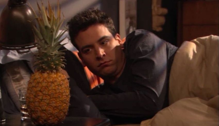 A man laying on a bed with a pineapple in front of him.