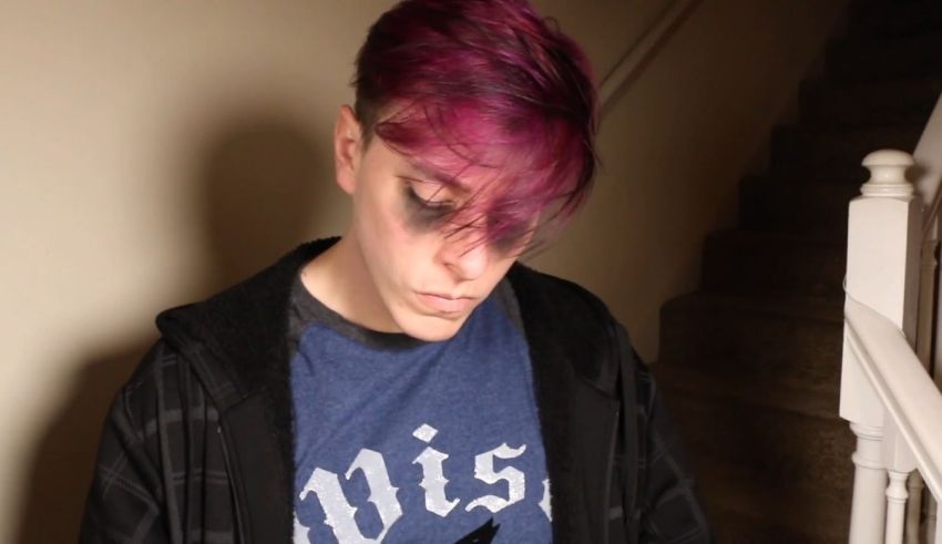 A young man with purple hair standing in front of stairs.