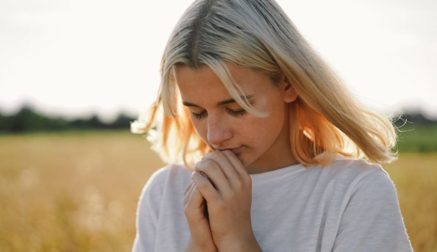 A young woman praying in a field.