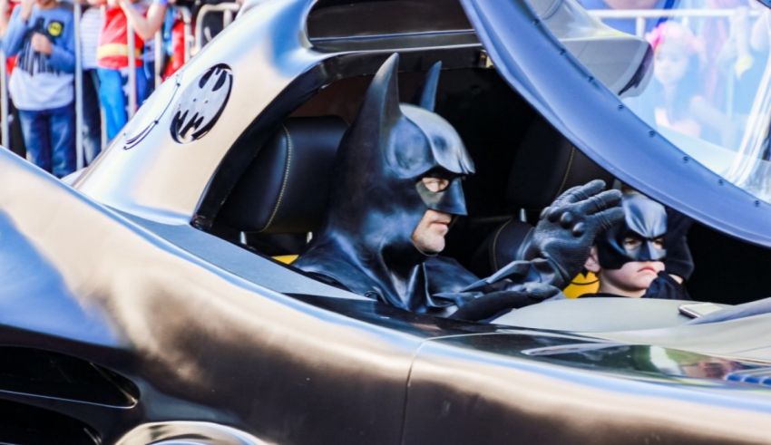 A man in a batman costume is driving a car.