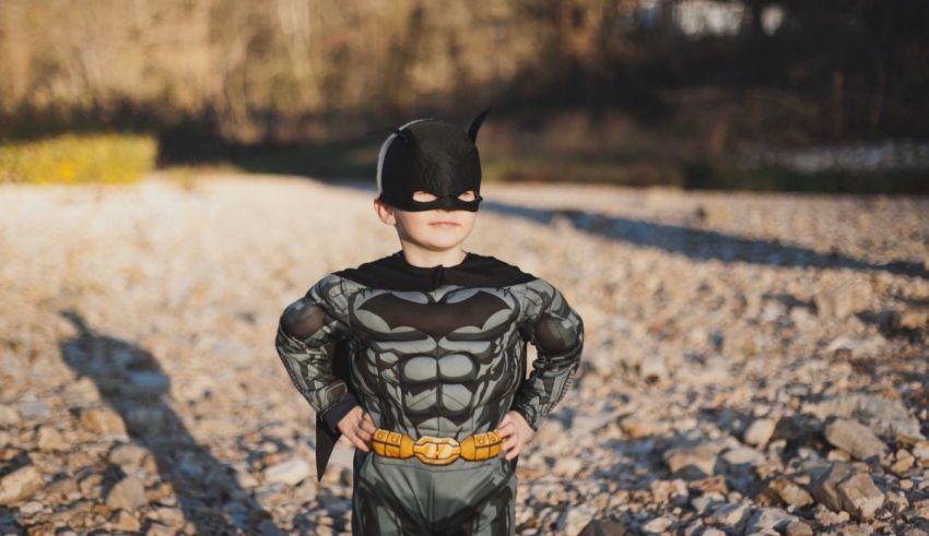A boy in a batman costume standing on rocks.