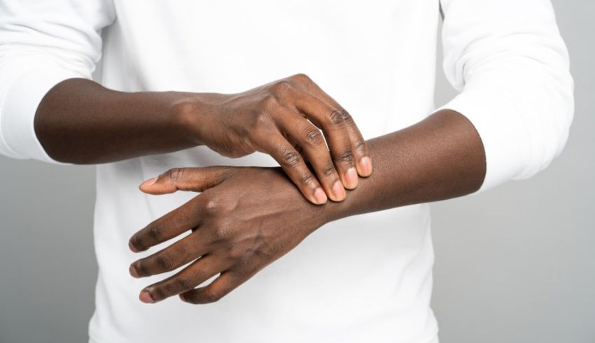 A black man is rubbing his hands on a gray background.