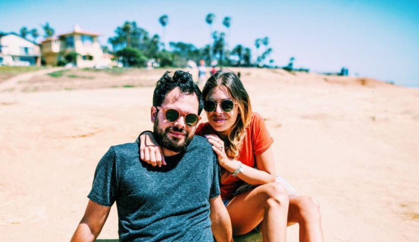 A man and woman sitting on a beach in sunglasses.