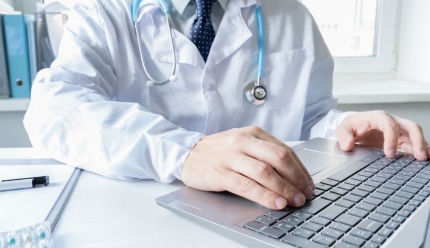 A doctor is typing on a laptop computer.