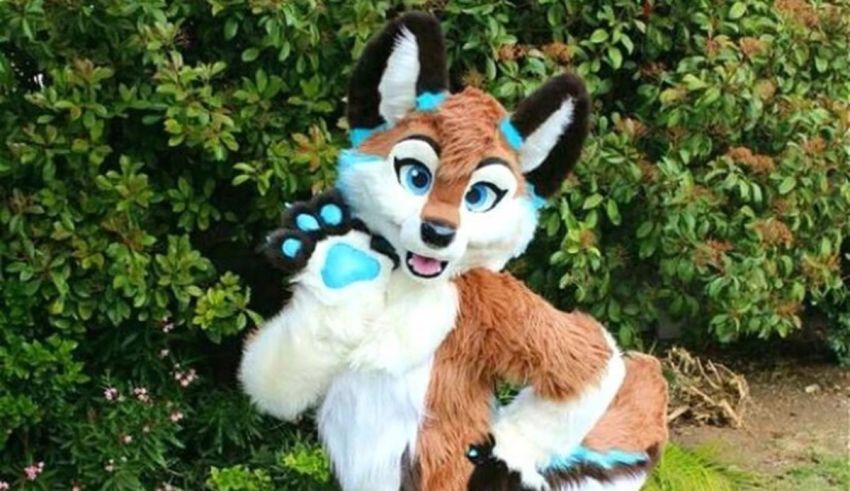 A fox mascot posing in front of bushes.