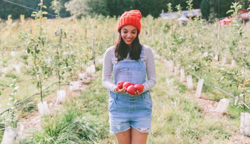 A young woman in overalls holding apples in an apple orchard.