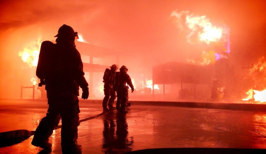A group of firefighters standing in front of a burning building.