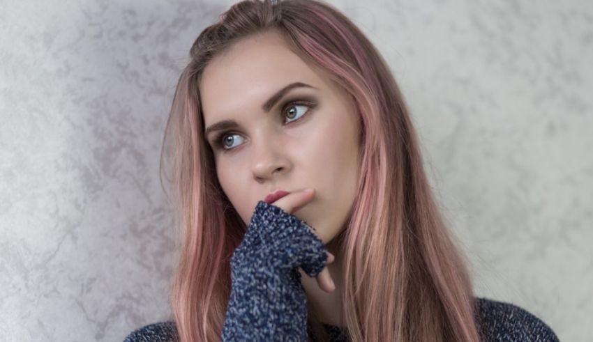 A young woman with pink hair leaning against a wall.