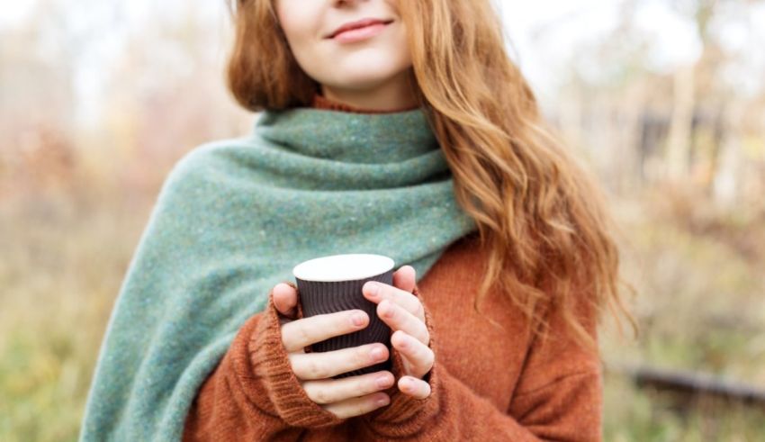 A woman is holding a cup of coffee outdoors.