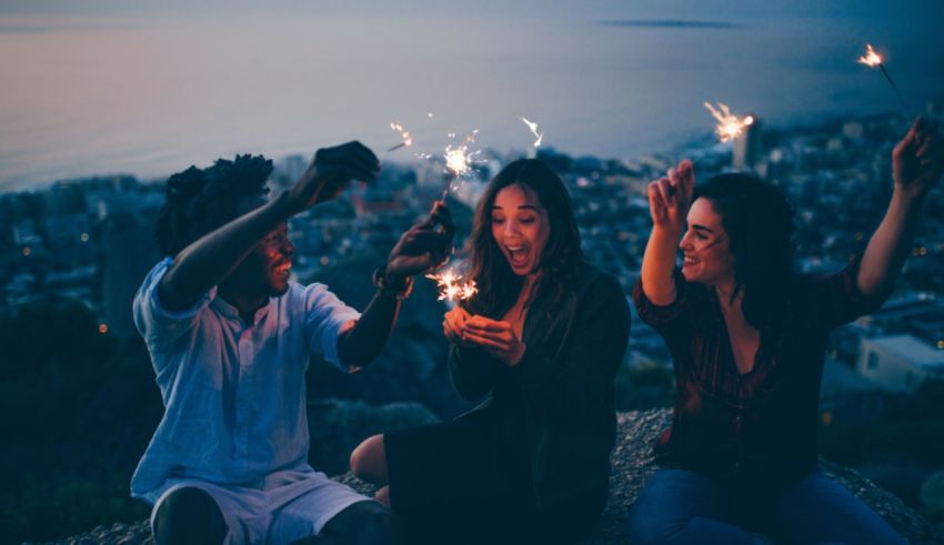 A group of friends holding sparklers while sitting on top of a hill.