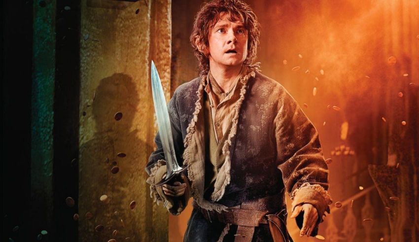 The hobbit is holding a sword in front of a fire.