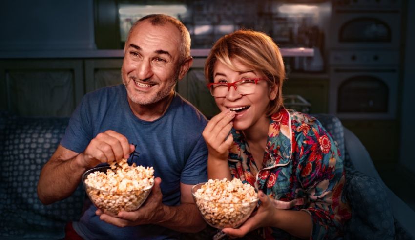 A man and woman sitting on a couch eating popcorn.