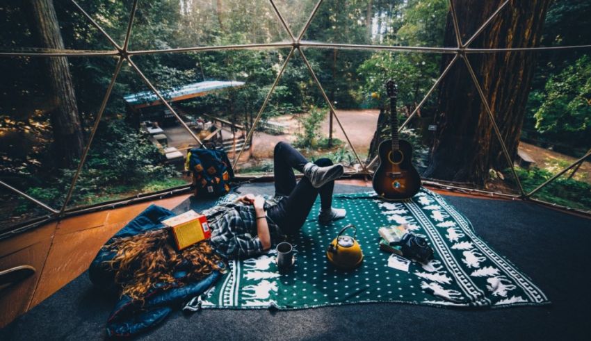 A woman laying on a blanket in a dome in the woods.