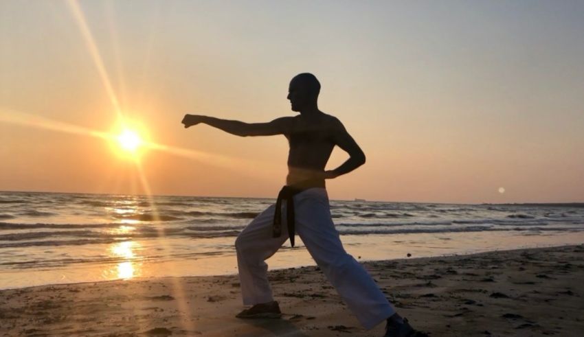 A man practicing karate on the beach at sunset.