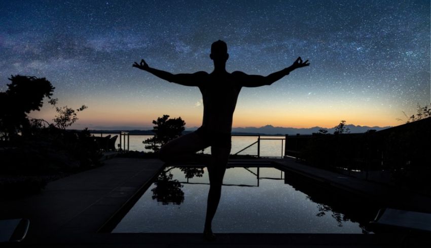 A silhouette of a man doing yoga in front of a pool at night.