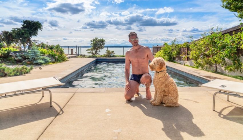 A man kneeling next to a pool with his dog.