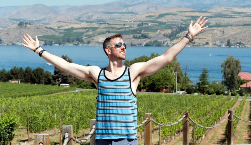 A man standing in front of a vineyard with his arms outstretched.