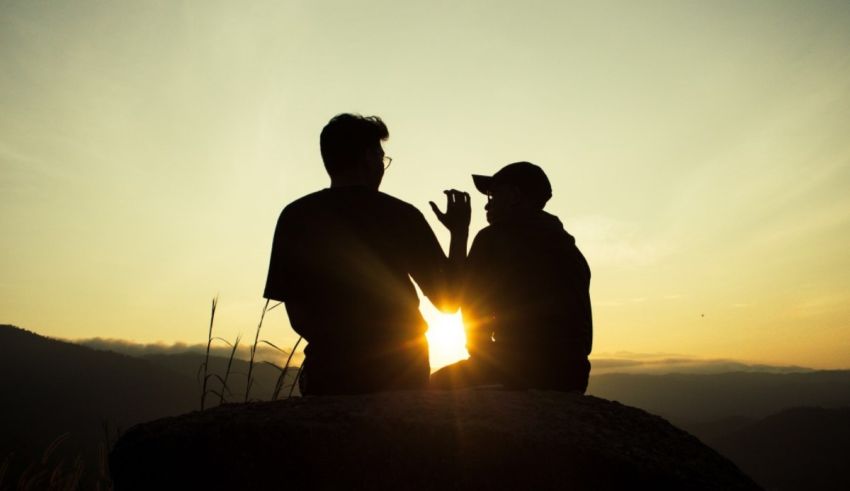 Two people sitting on top of a mountain at sunset.