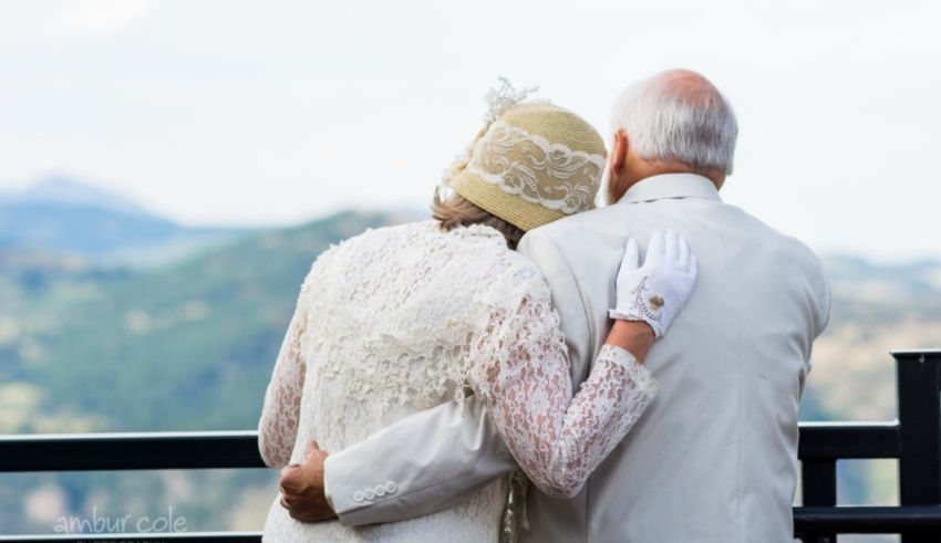 An older couple hugging on a balcony overlooking the mountains.