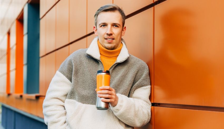 A man holding a coffee cup in front of an orange wall.