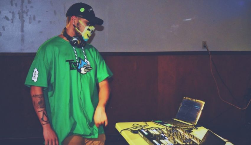 A man in a green shirt with a mask in front of a dj booth.