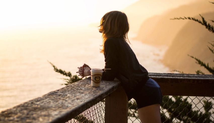 A woman is sitting on a railing overlooking the ocean.