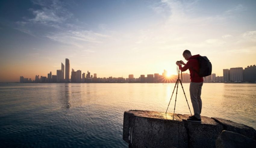 A man with a backpack is taking a picture of the city at sunset.