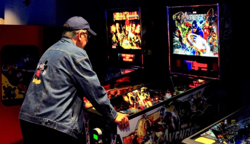 A man playing a pinball machine in a game room.