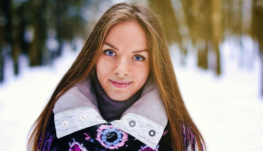 A young woman with long hair and blue eyes is posing in the snow.