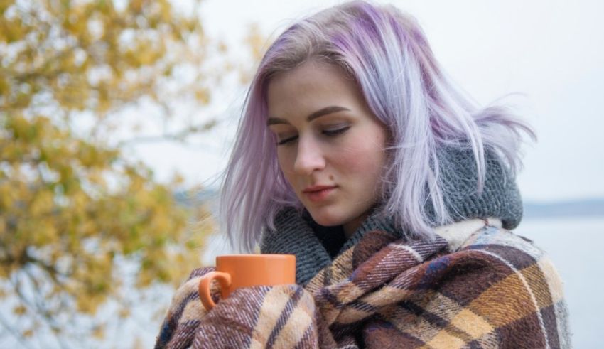 A woman with purple hair is holding a coffee mug.