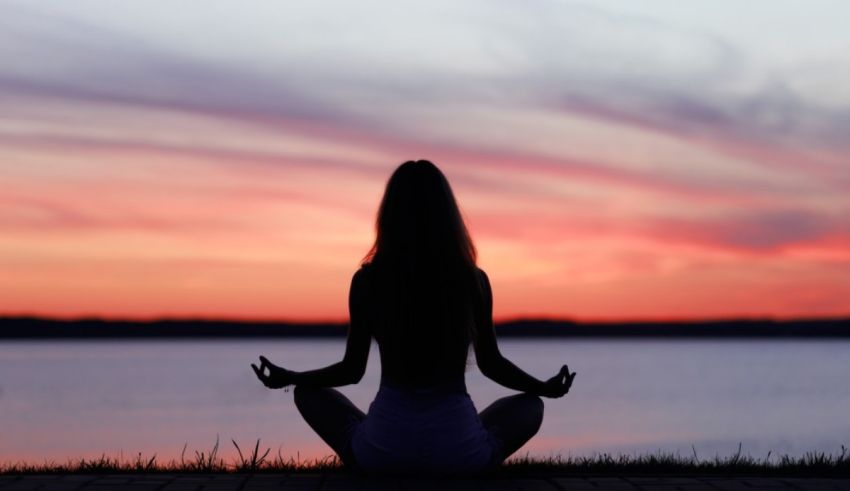 A woman is meditating in front of a lake at sunset.