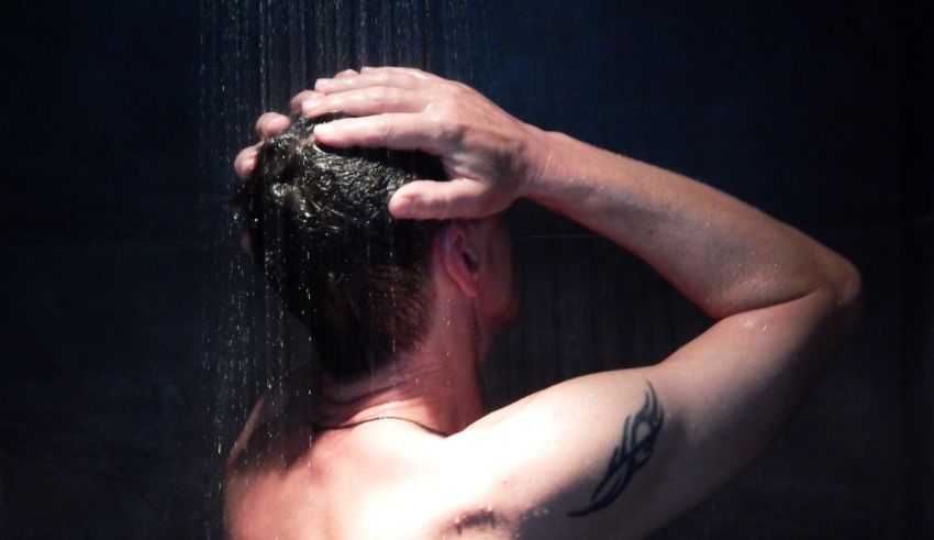 A man taking a shower with a tattoo on his back.