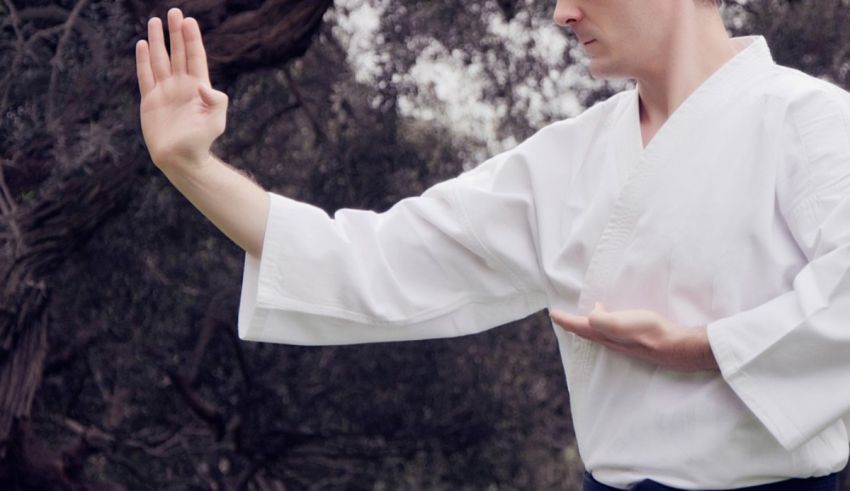 A man in a white karate kimono is doing a hand gesture.