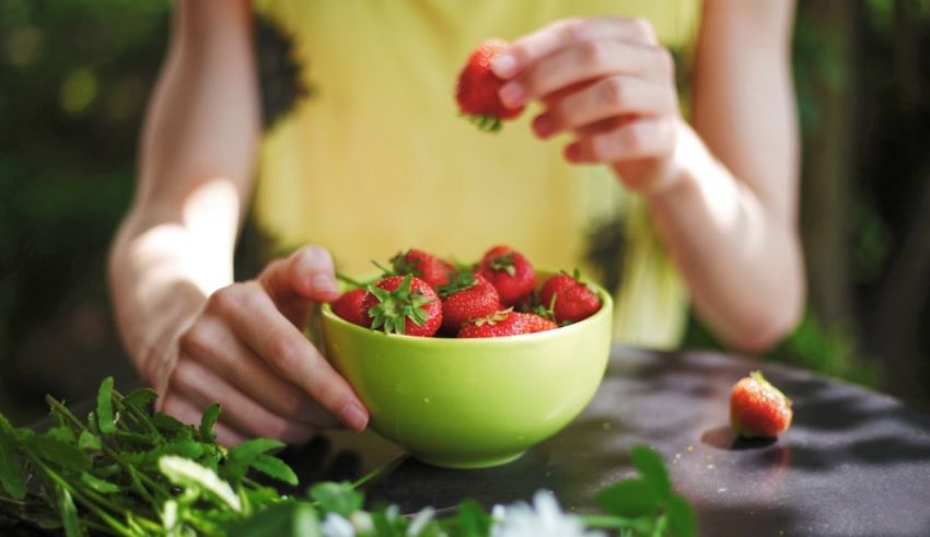 A woman is picking strawberries out of a green bowl.