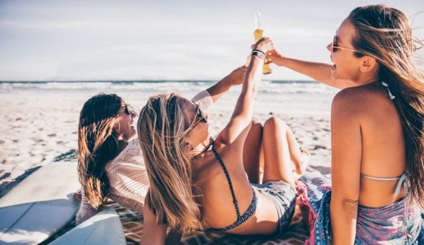 Three women toasting on the beach with surfboards.