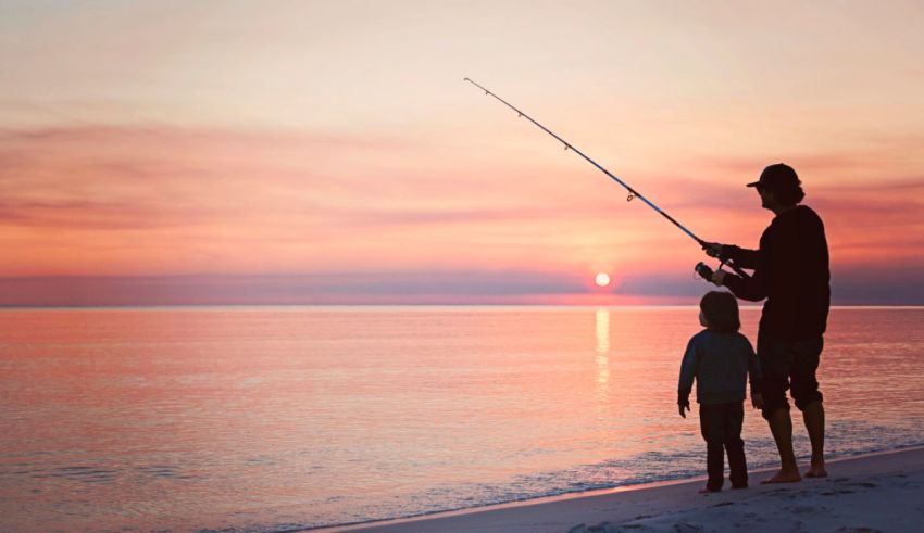 A man and a child fishing on the beach at sunset.