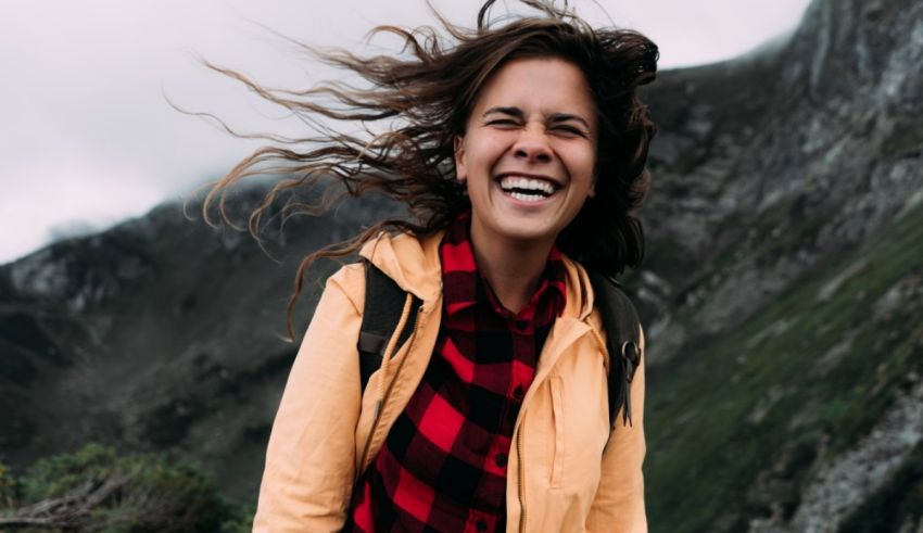 A woman laughing in the mountains with her hair blowing in the wind.