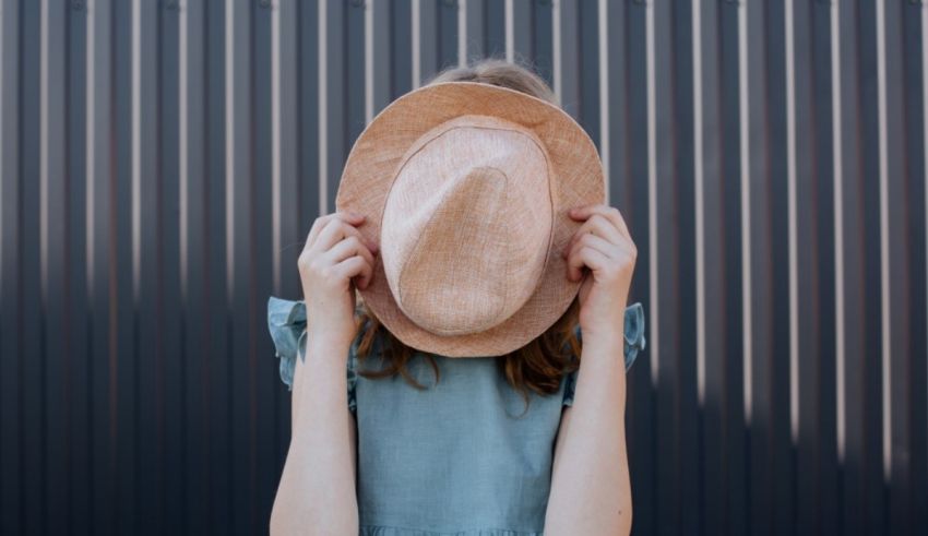 A young girl wearing a hat in front of a wall.