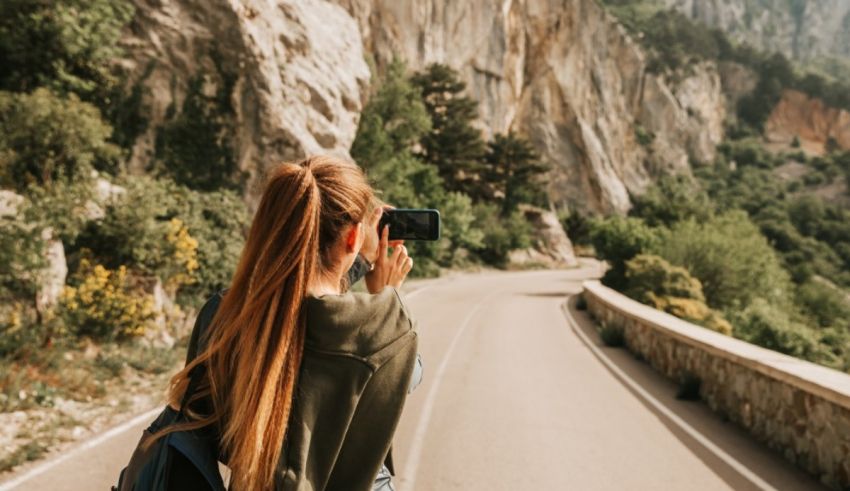 A woman is taking a picture of a mountain road.