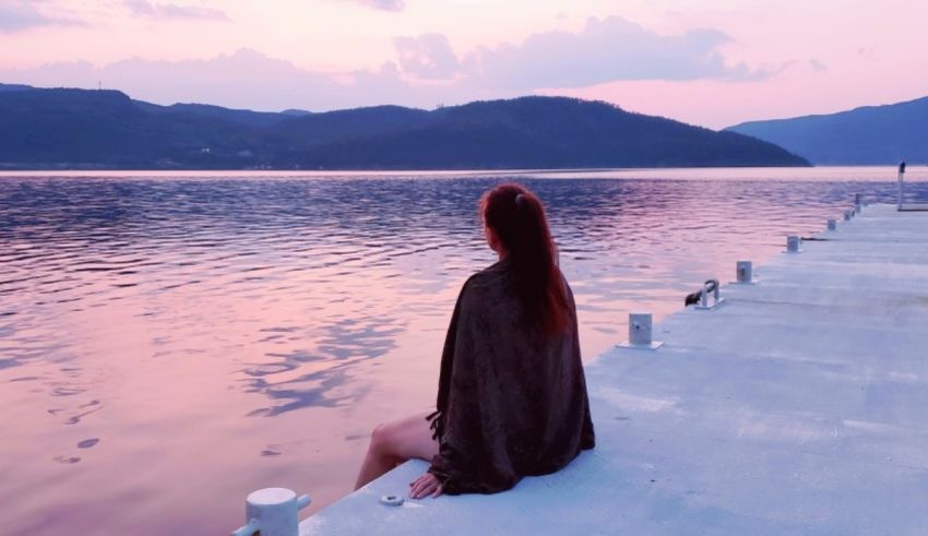 A woman sitting on a dock looking at a lake at sunset.