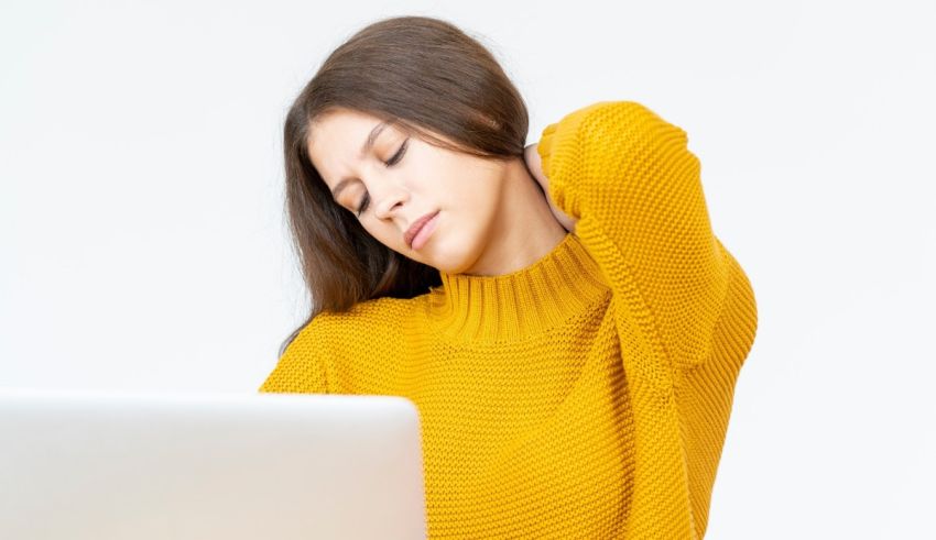 A woman wearing a yellow sweater is working on a laptop.