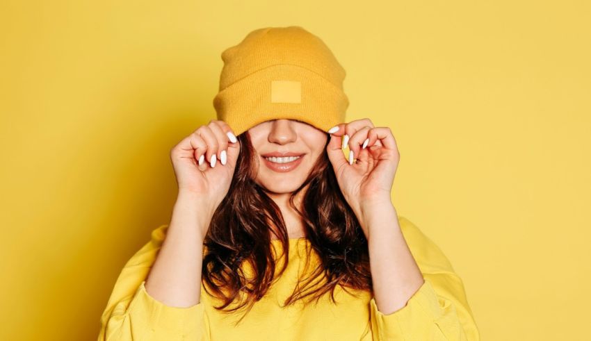 A woman wearing a yellow beanie covering her eyes on a yellow background.