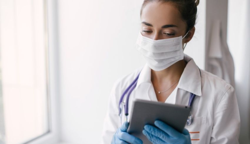 A female doctor wearing a mask and gloves is using a tablet.