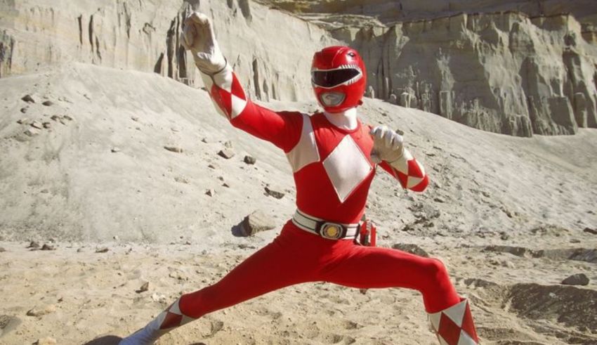 A red and white power ranger poses in the sand.