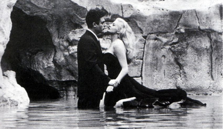 A black and white photo of a man and woman kissing in the water.