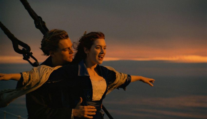 A couple on the deck of a ship with their arms outstretched.
