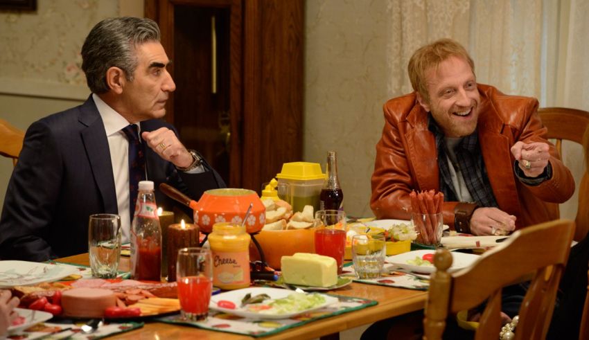 Two men sitting at a table with food and drinks.